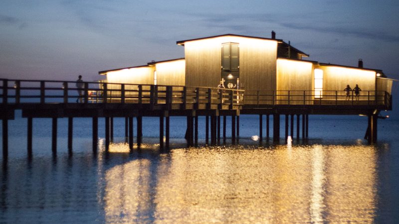 Båstad’s illuminated cold-bath house on a pier above the sea at dusk, photographed in 2014.